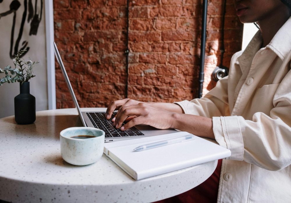 Woman working on a laptop in a coffee shop with a drink on the table, following laptop etiquette in a café setting