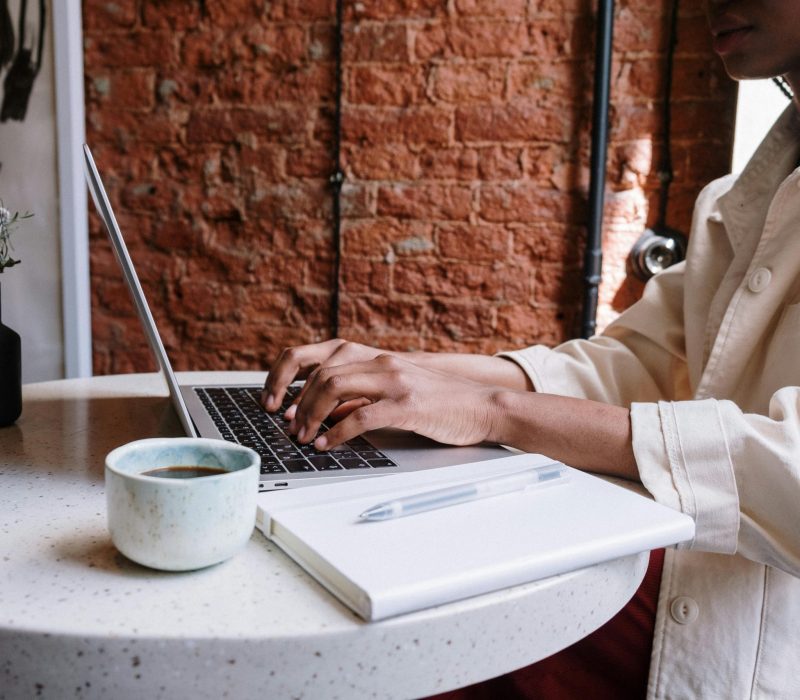 Woman working on a laptop in a coffee shop with a drink on the table, following laptop etiquette in a café setting